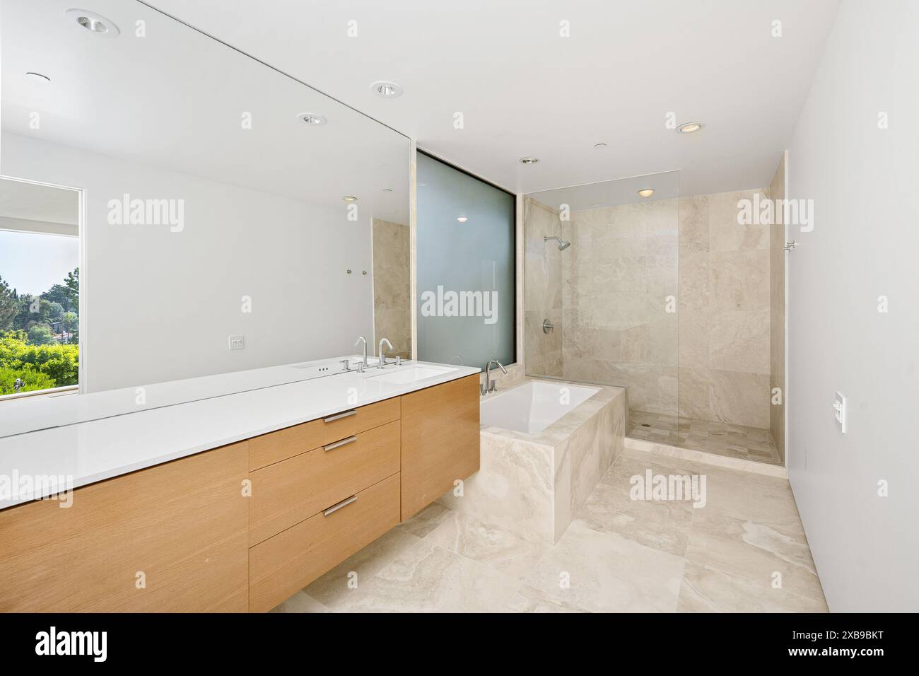 Un bagno spazioso e contemporaneo con arredi in legno, lavandini bianchi e pareti Foto Stock