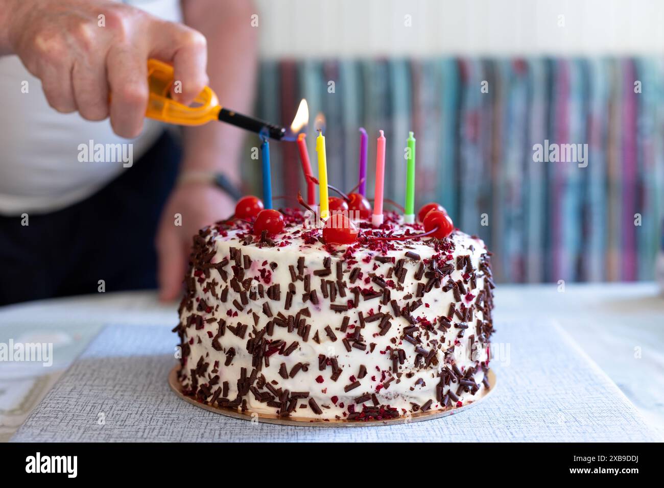 Torta della Foresta Nera con ciliegie, gocce di cioccolato e panna montata. Torta di compleanno. L'uomo accende le candele. Torta di ciliegie Shvartsvald. Foto Stock