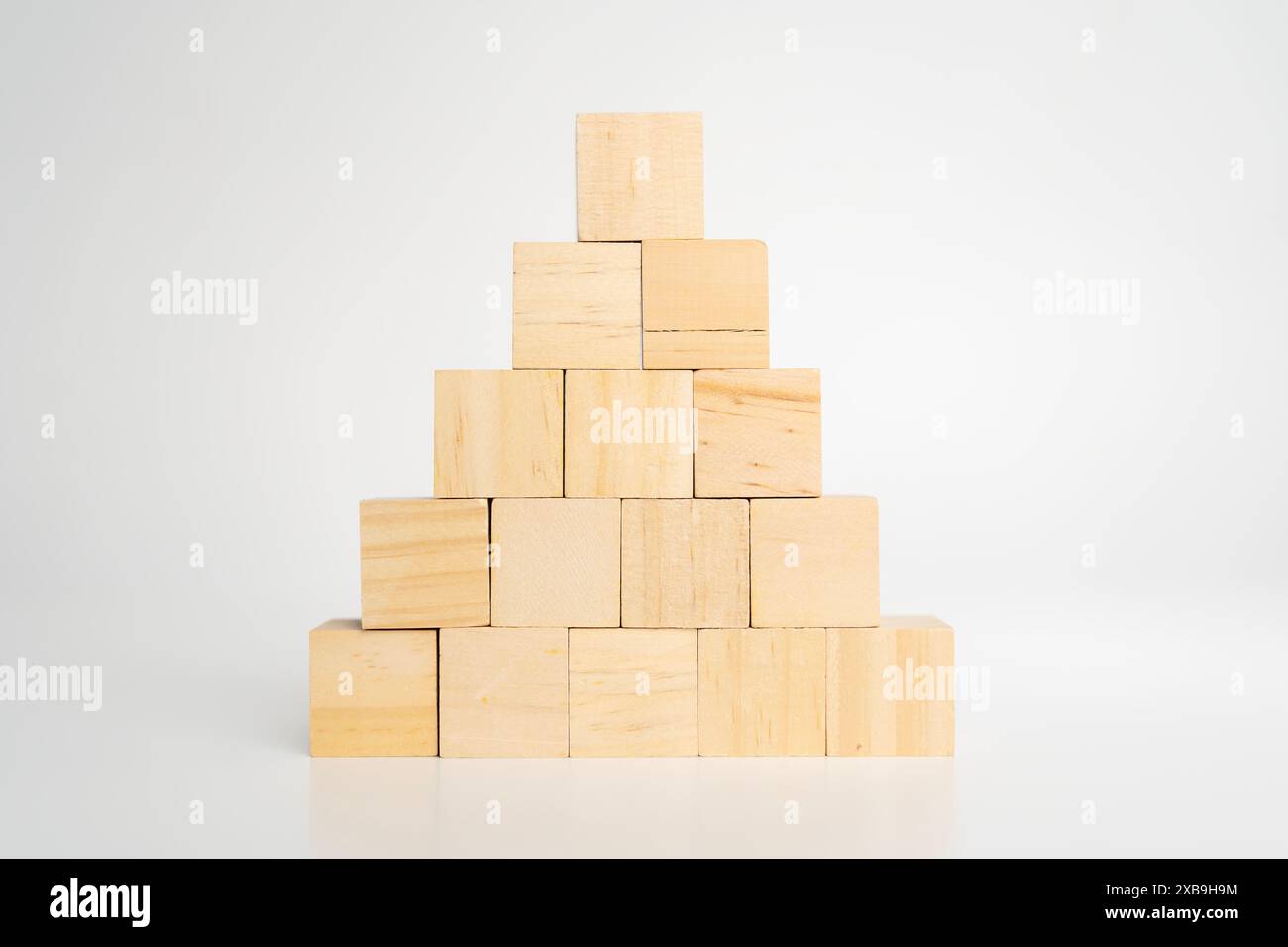 I blocchi vuoti vuoti di legno a cubo costruiscono una forma piramidale con quello grande in cima, isolato su una scrivania di legno su sfondo bianco. Processo di crescita aziendale, formazione Foto Stock