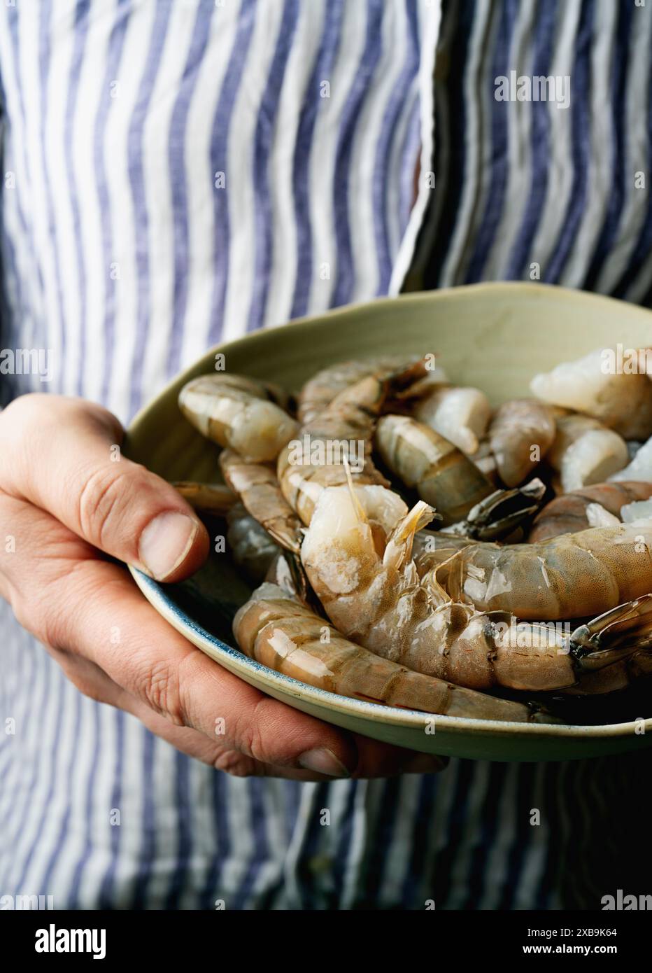 Gamberi freschi tenuti in una ciotola da una persona che indossa una camicia a righe. I gamberi sono crudi e hanno un aspetto lucido e traslucido, a indicare la loro freschezza Foto Stock