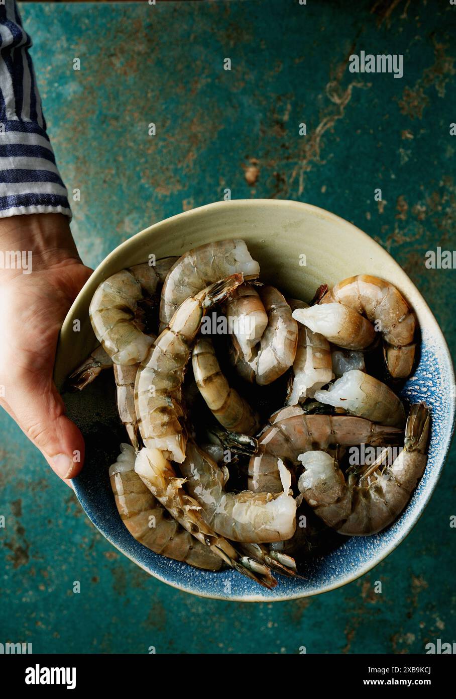 Recipiente di gamberi freschi e crudi. Sfondo blu. Gamberi di varie dimensioni, pronti per la preparazione. Foto Stock