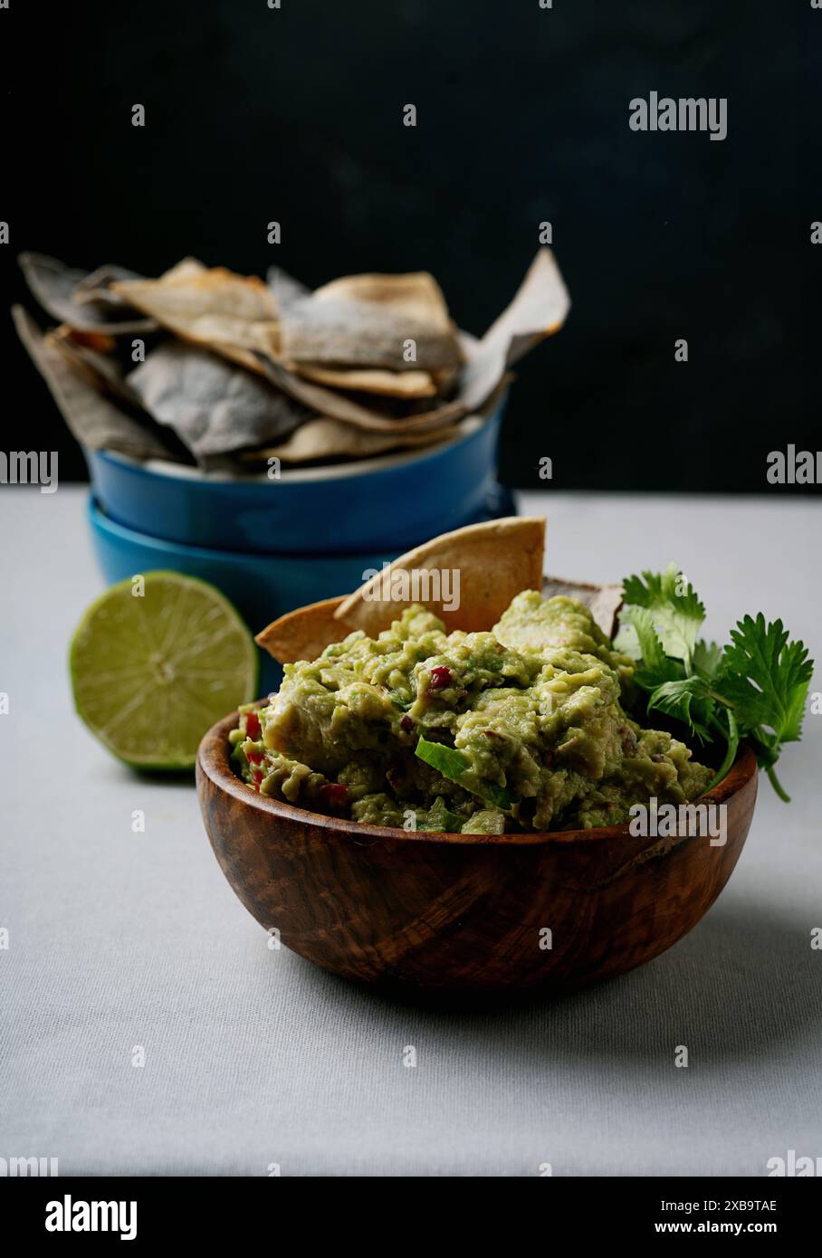 Primo piano di una ciotola di legno riempita di guacamole, guarnita con coriandolo e circondata da patatine. Foto Stock