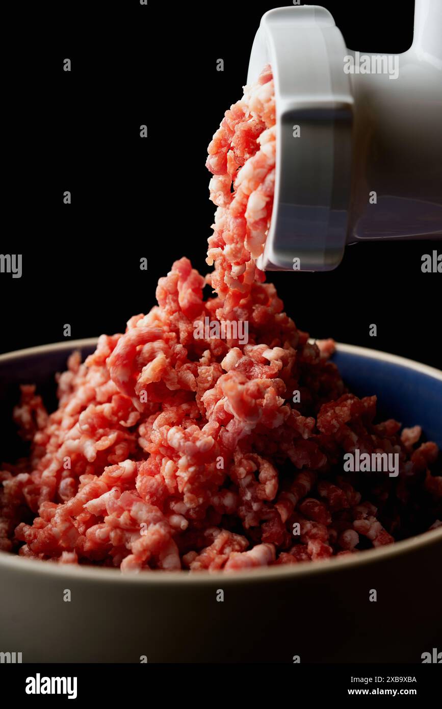 Foto ravvicinate della carne macinata che emerge da un macinacaffè. La carne macinata è fresca e cruda, con particolare attenzione alla consistenza e al colore su uno sfondo scuro Foto Stock