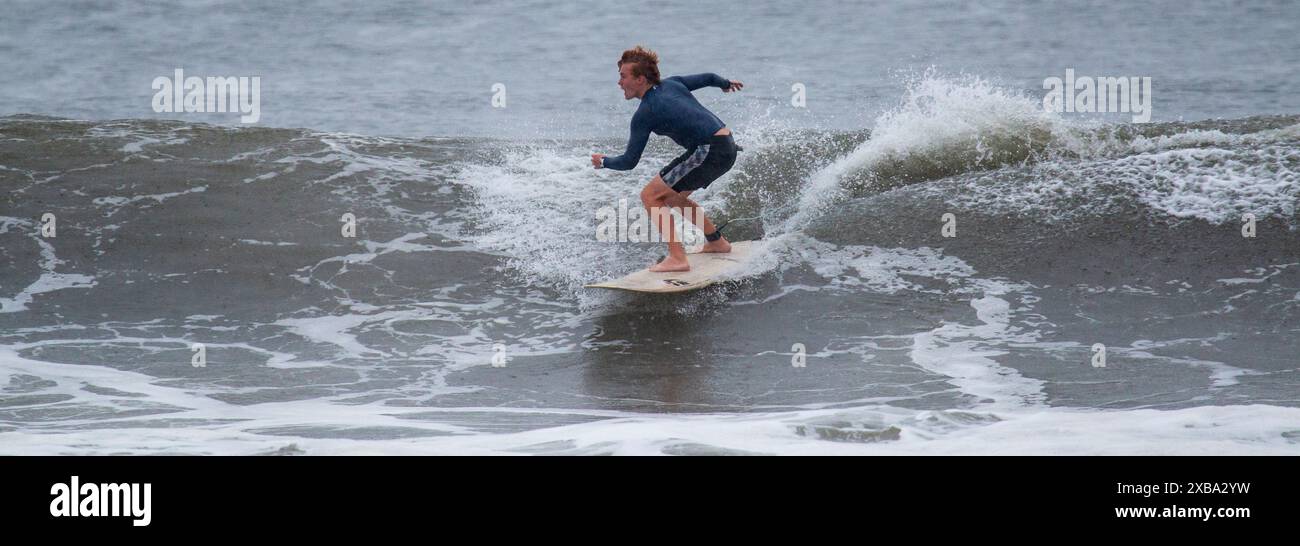 Gilgo Beach, New York, USA - 30 agosto 2023: Un surfista maschio che naviga in un'onda sotto la pioggia con l'uragano Franklin al largo della costa di Long Island. Foto Stock