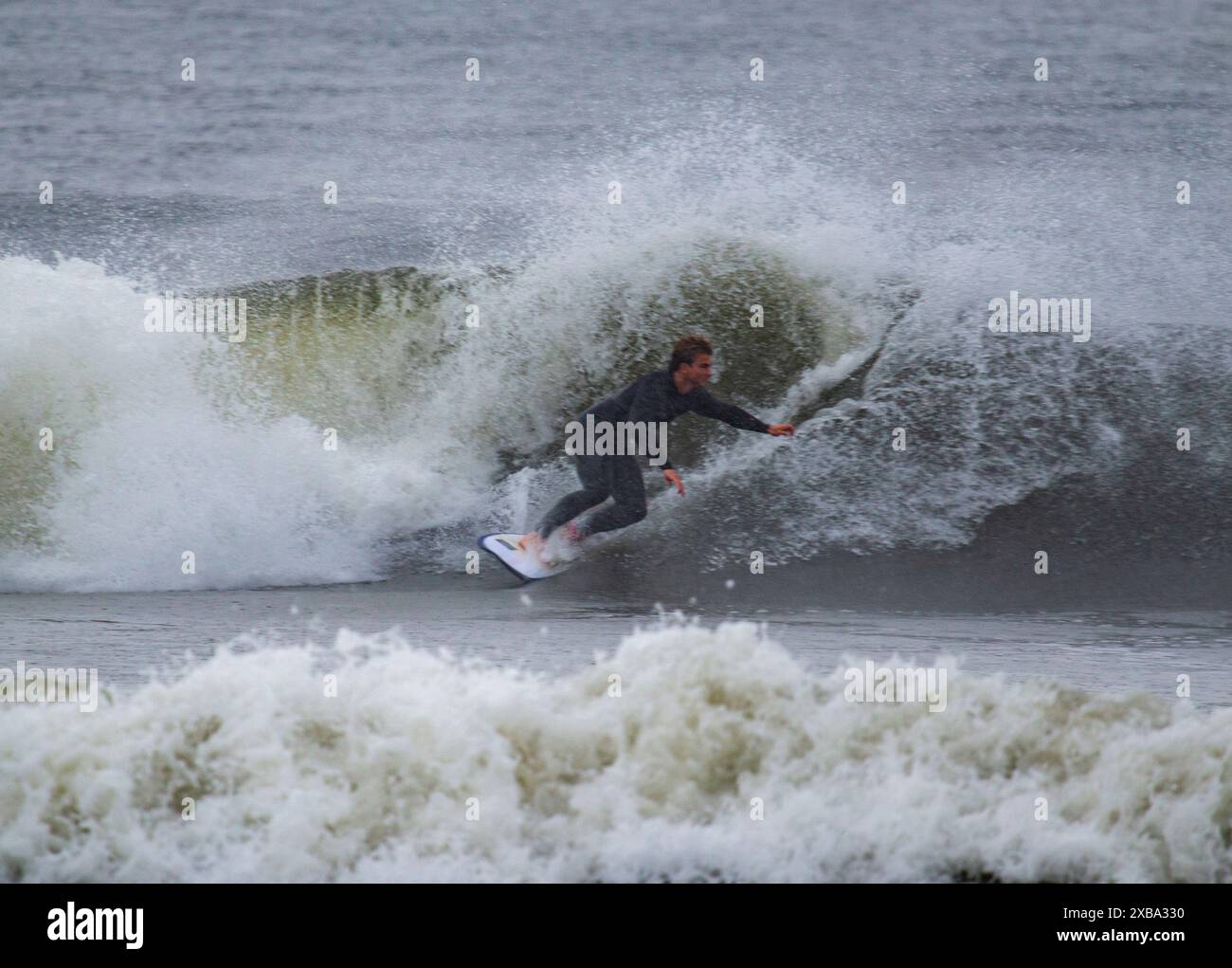 Gilgo Beach, New York, Stati Uniti d'America - 30 agosto 2023: Un surfista maschio che fa surf con un'onda ruvida sotto la pioggia con l'uragano Franklin al largo della costa di Long Island. Foto Stock