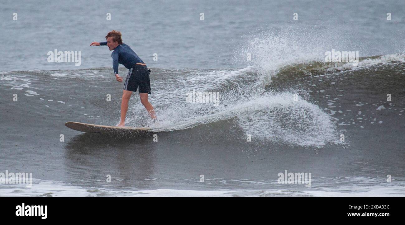 Gilgo Beach, New York, USA - 30 agosto 2023: Un surfista maschio che naviga in un'onda sotto la pioggia con l'uragano Franklin al largo della costa di Long Island. Foto Stock