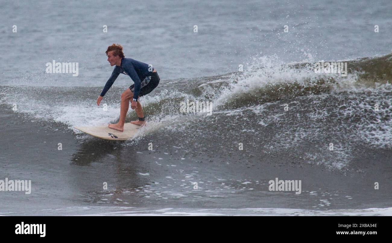 Gilgo Beach, New York, USA - 30 agosto 2023: Un surfista maschio che naviga in un'onda sotto la pioggia con l'uragano Franklin al largo della costa di Long Island. Foto Stock