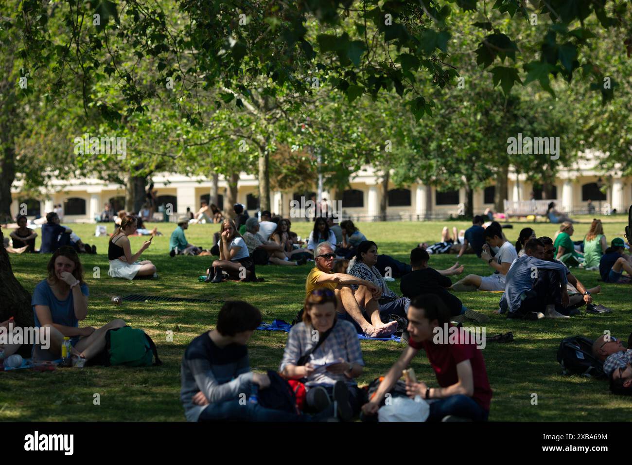 Le persone godono di un periodo di caldo, mentre alcuni prendono il sole e altri evitano il sole diretto a St James's Park, Londra. Foto Stock