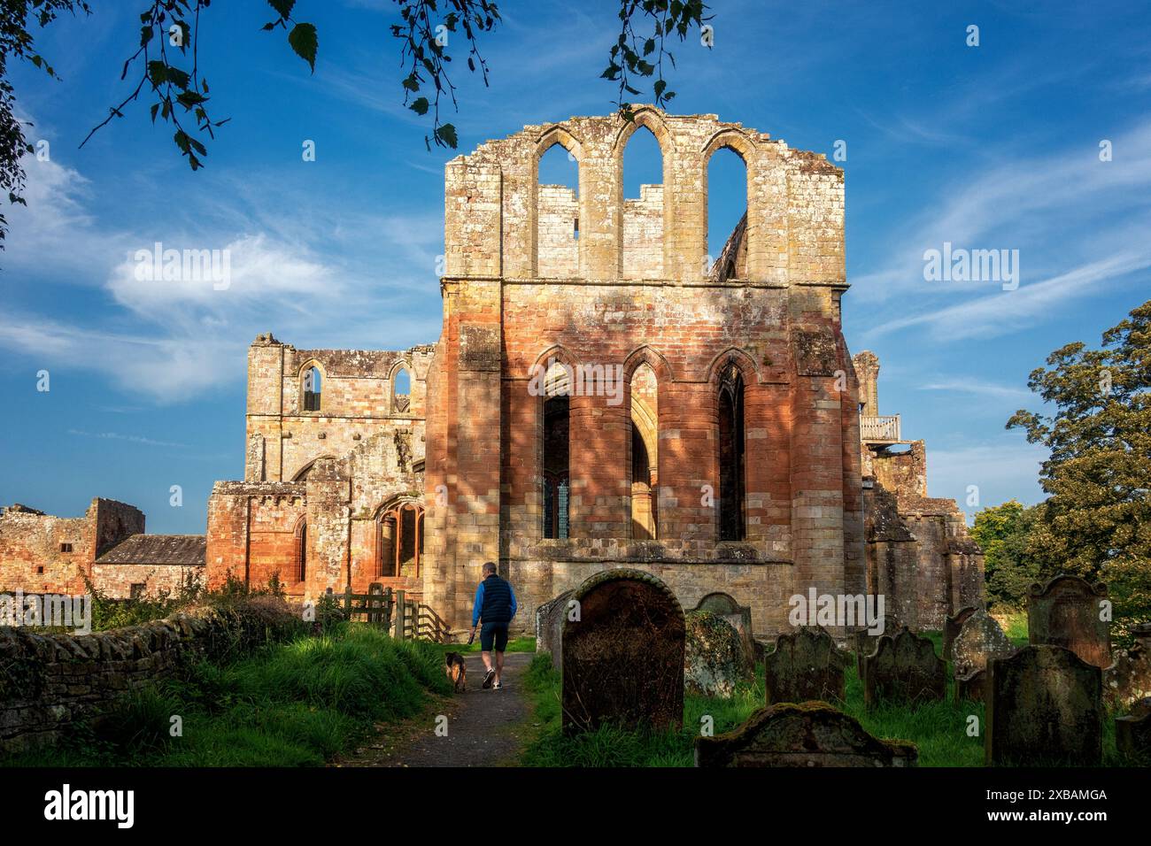 Lanercost Priory alla luce del sole con un passerella per cani che cammina nel cimitero di Cumbria, Inghilterra, Regno Unito Foto Stock