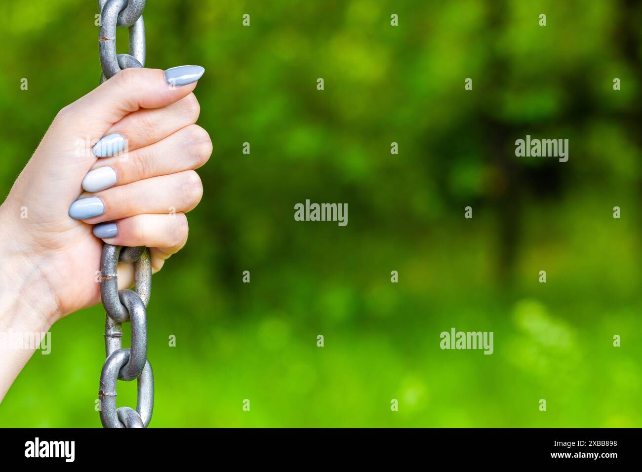 mano femminile che tiene una catena metallica, primo piano. mano che regge una catena metallica. relazioni abusive. supporto affidabile. psicologia della dipendenza Foto Stock