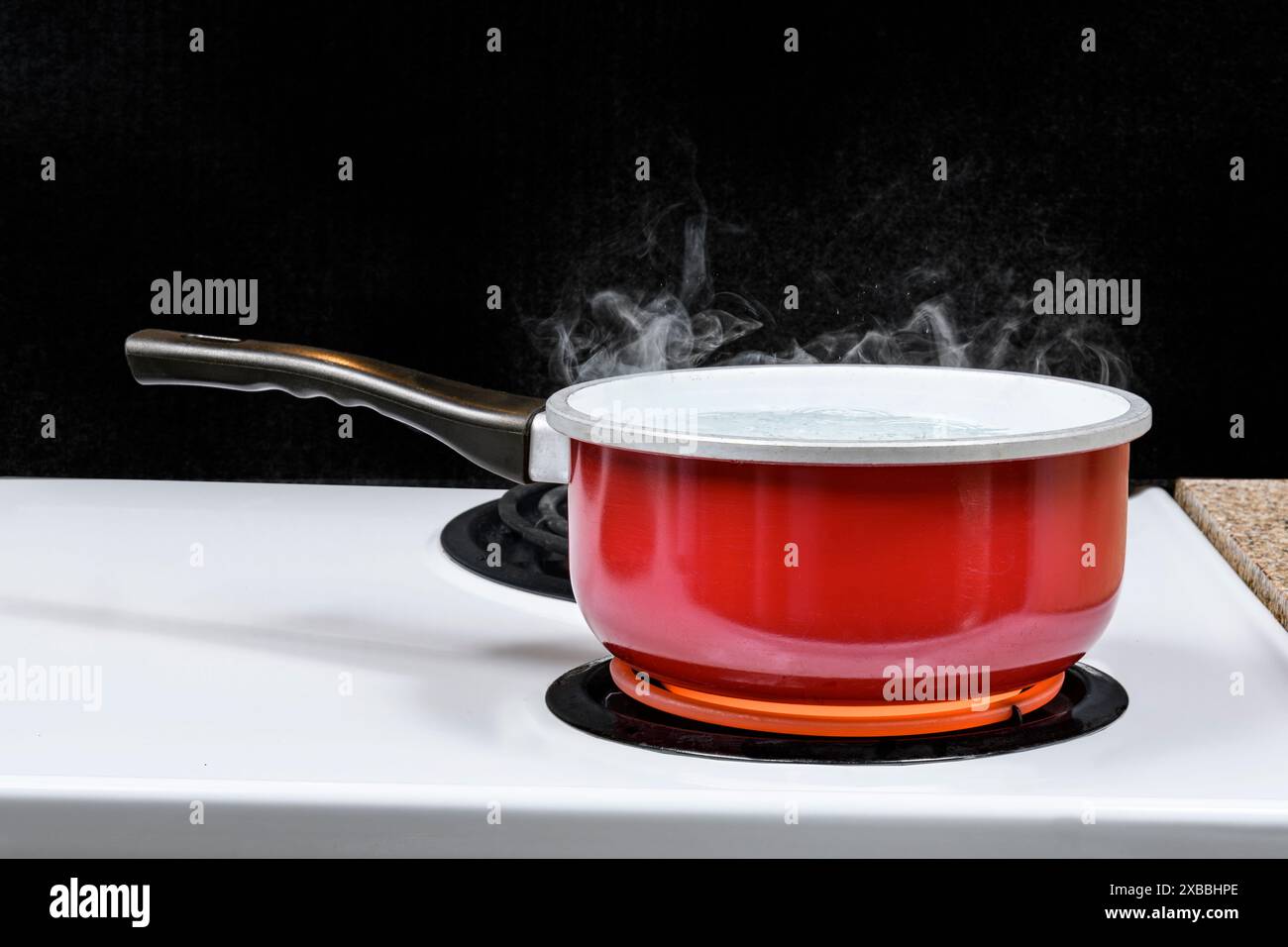 Colpo orizzontale di una pentola rossa di acqua bollente su una stufa elettrica con sfondo nero. Copia spazio. Foto Stock