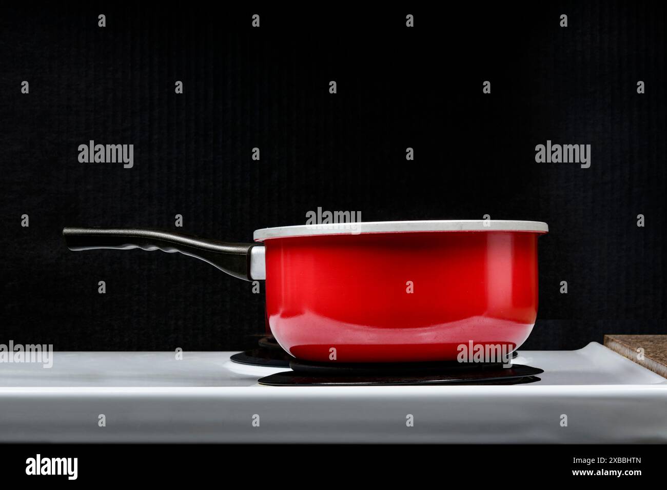 Colpo orizzontale di una pentola rossa su un fornello elettrico con sfondo nero. Vista laterale. Copia spazio. Foto Stock