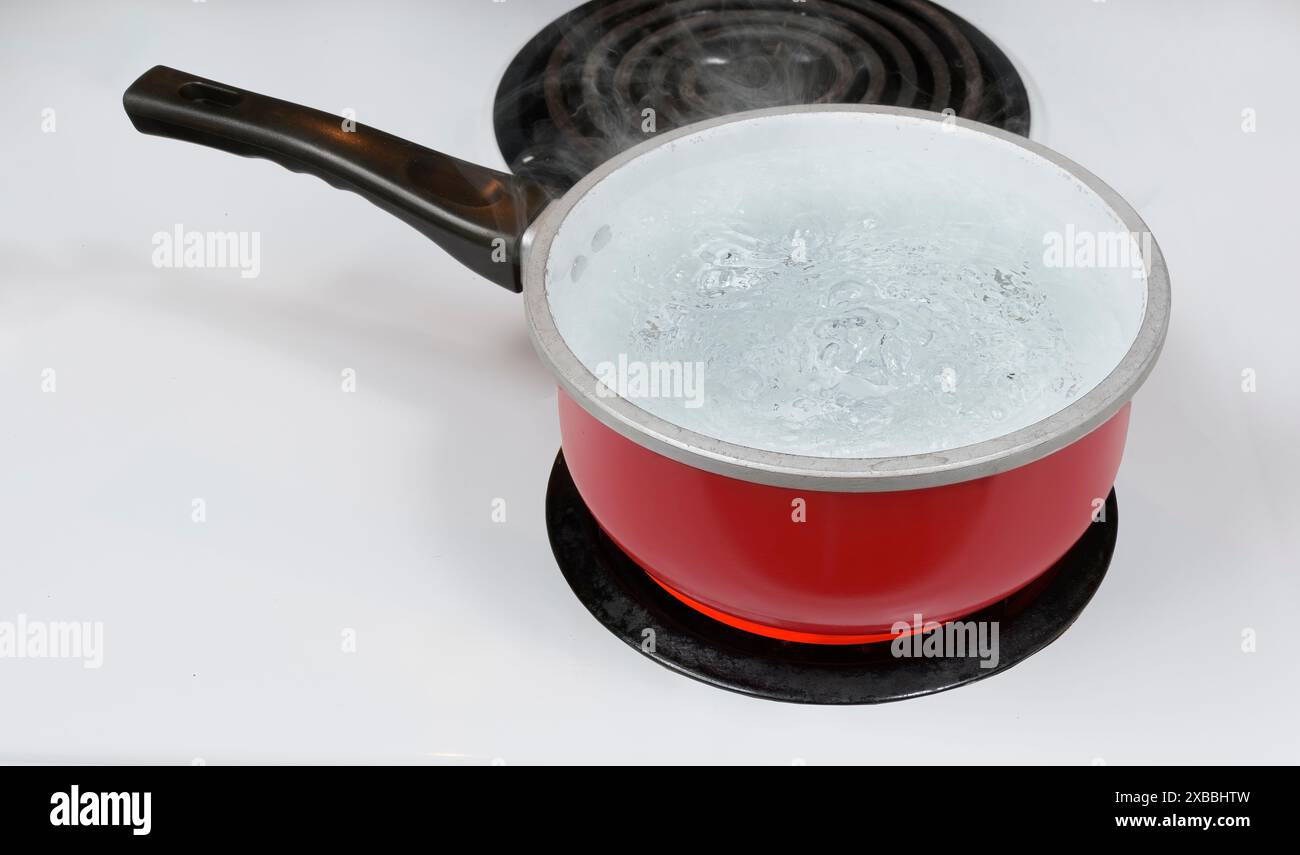 Colpo orizzontale rivolto verso il basso su una pentola rossa di acqua bollente su un fornello elettrico. Foto Stock