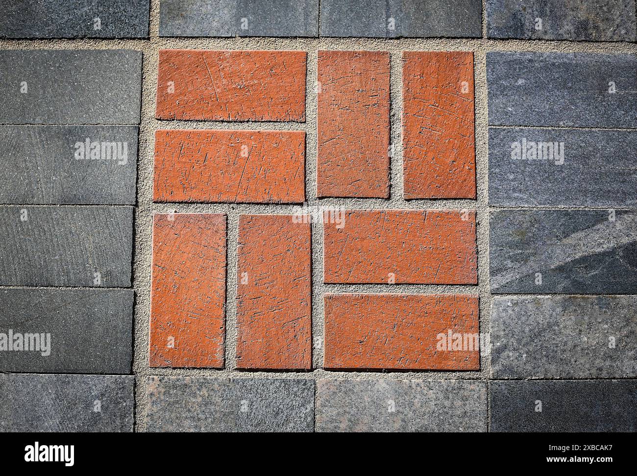 Motivo geometrico con mattoni rossi circondati da piastrelle grigie in cemento, immagine di sfondo Foto Stock