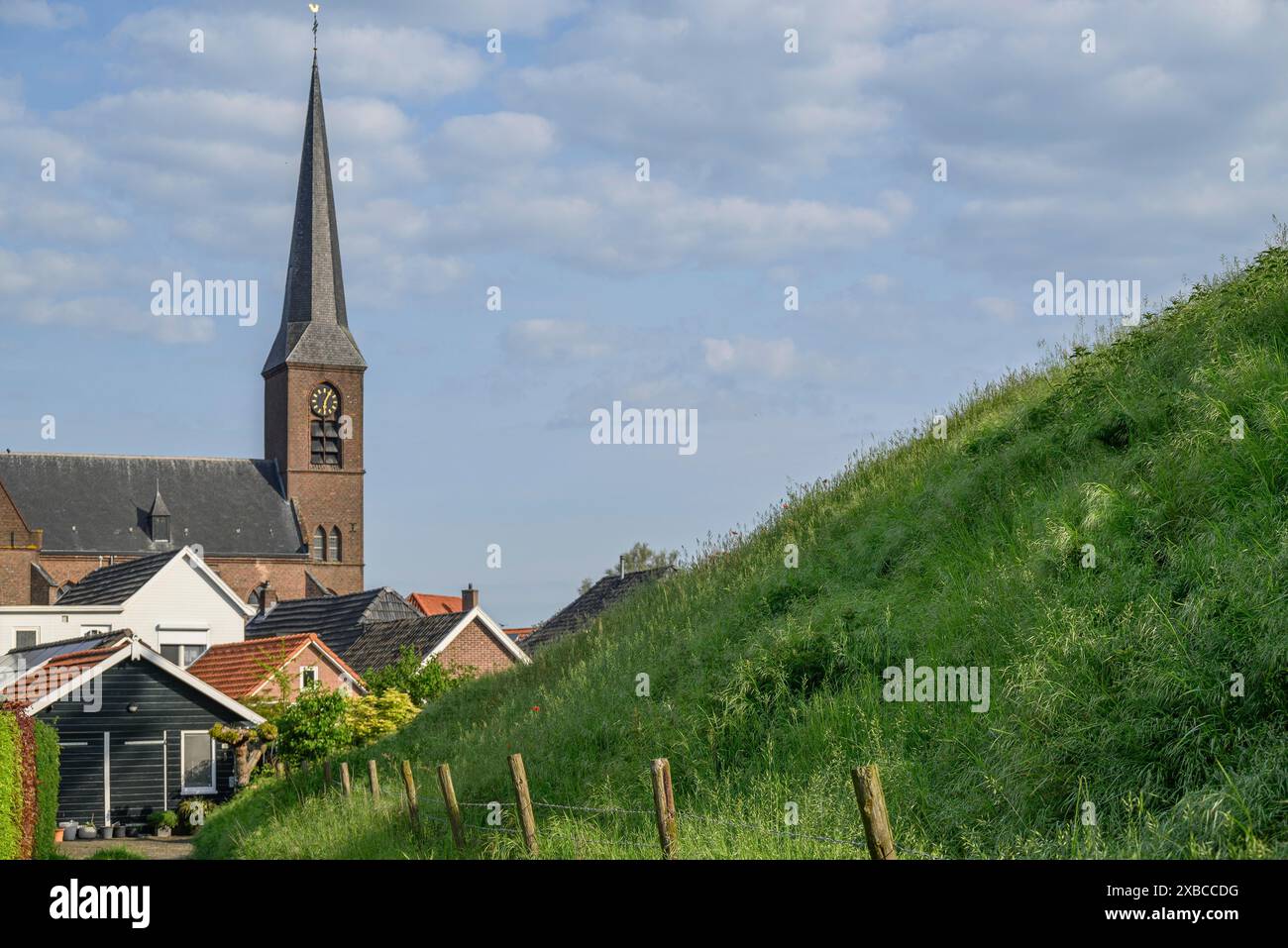 Scenario rurale con una chiesa sullo sfondo, una ripida collina verde e case tranquille con il sole, Bredevoort, gelderlande, paesi bassi Foto Stock