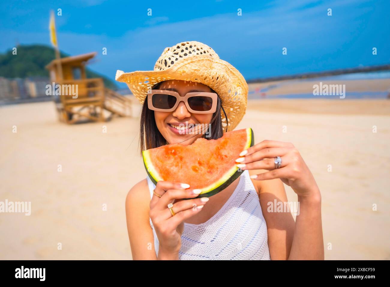 Una donna sorride e tiene una fetta di anguria su una spiaggia. Concetto di relax e divertimento all'aperto Foto Stock