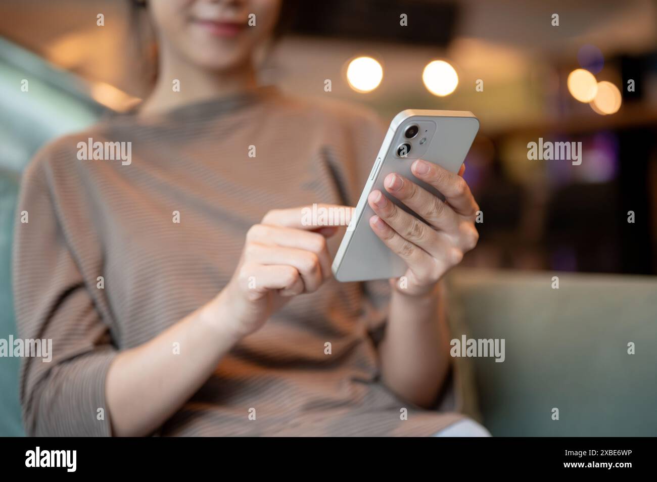 Un'immagine ritagliata di una giovane donna asiatica positiva che usa il suo smartphone mentre si siede su un divano in una lounge dell'hotel o in una caffetteria. persone e wireless t Foto Stock