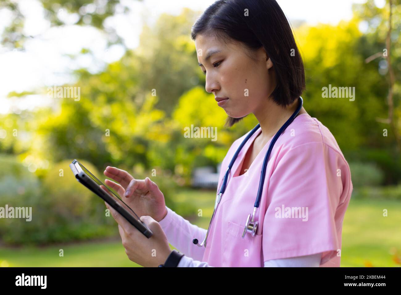 Infermiera asiatica operatore sanitario che utilizza un tablet in giardino, a casa Foto Stock