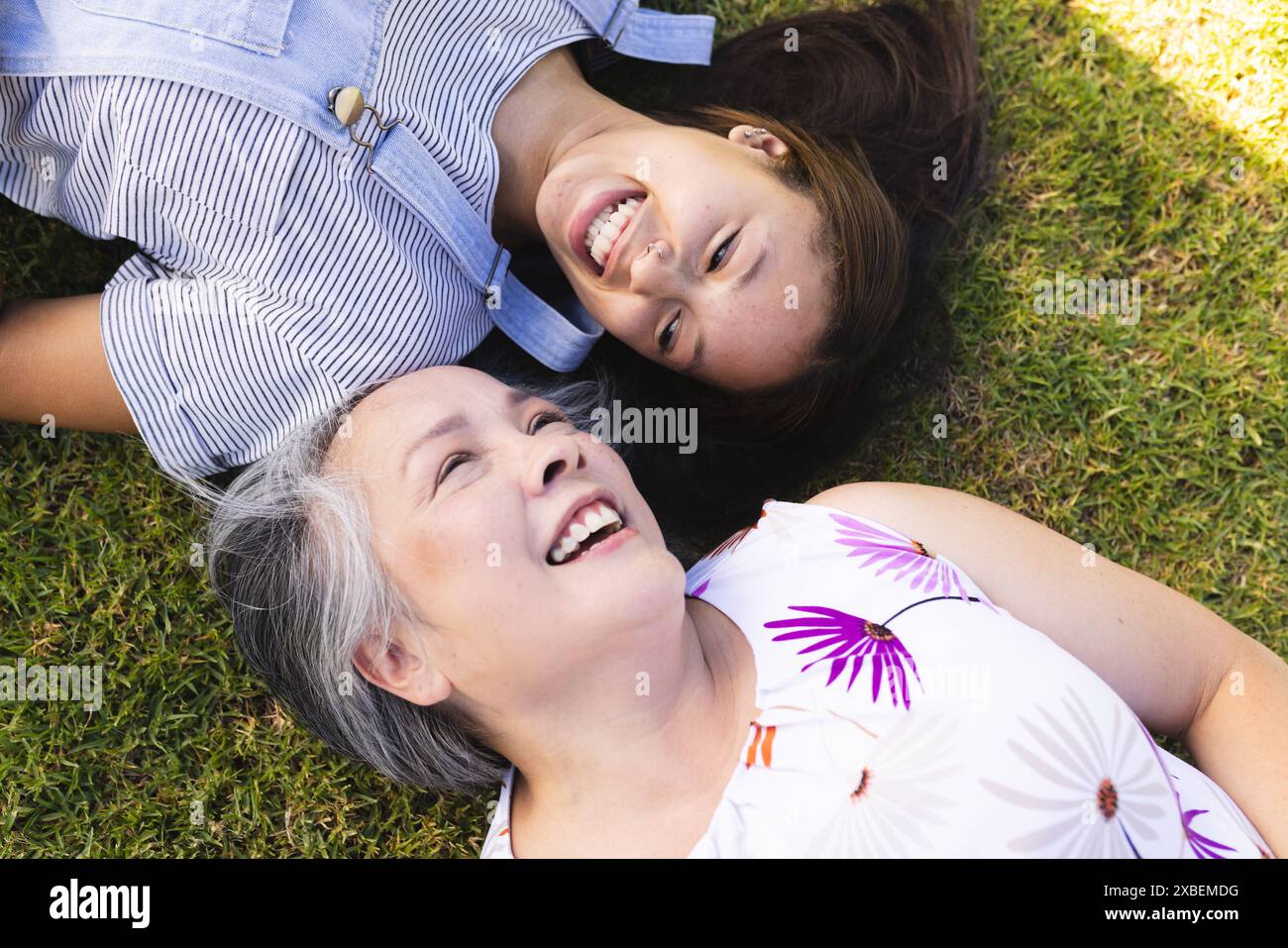 Nonna asiatica e nipote birazziale sdraiata sull'erba, sorridente e divertendosi Foto Stock
