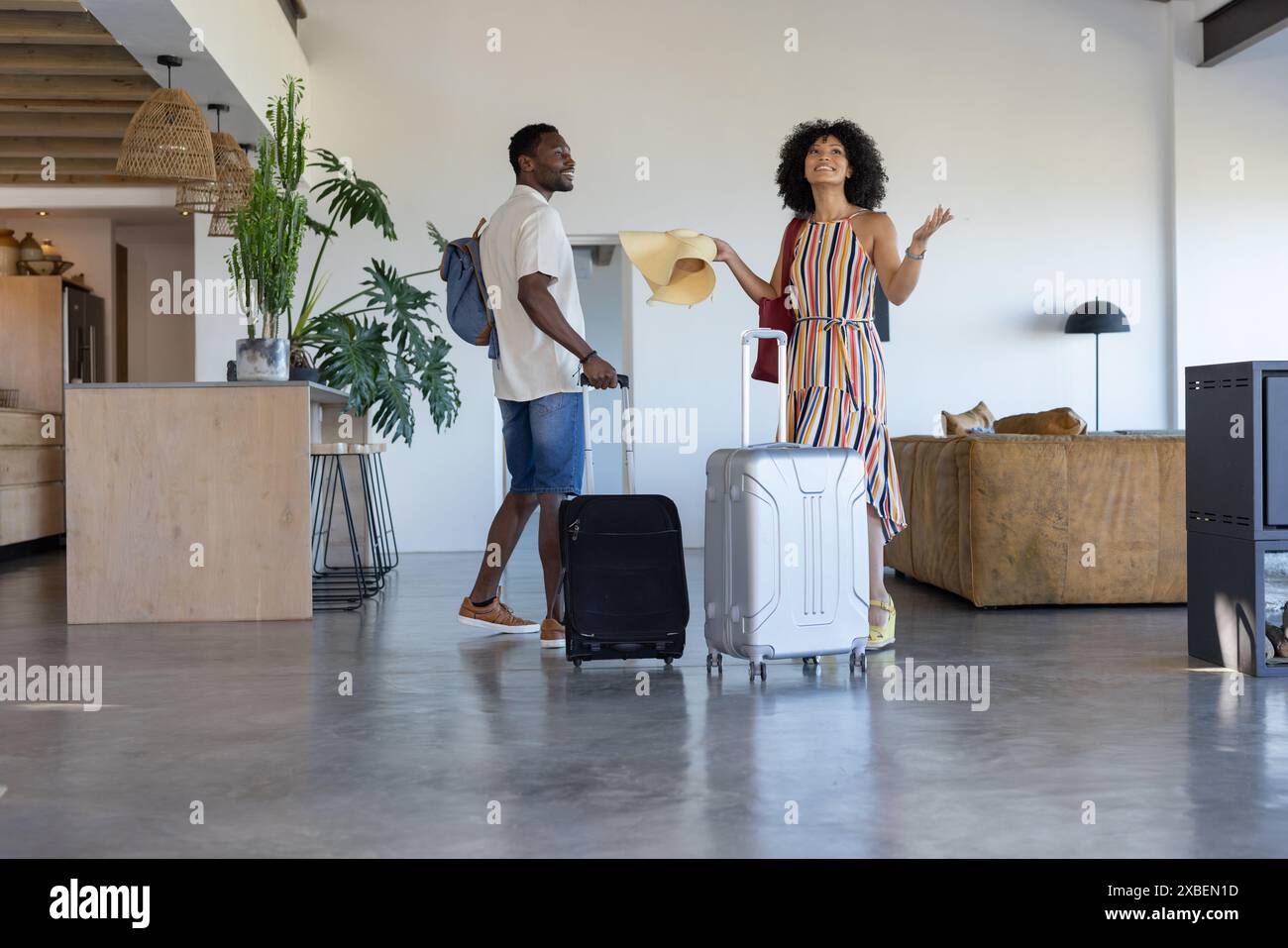 Una coppia variegata si trova in una moderna casa vacanze con valigie, che sembra eccitata Foto Stock