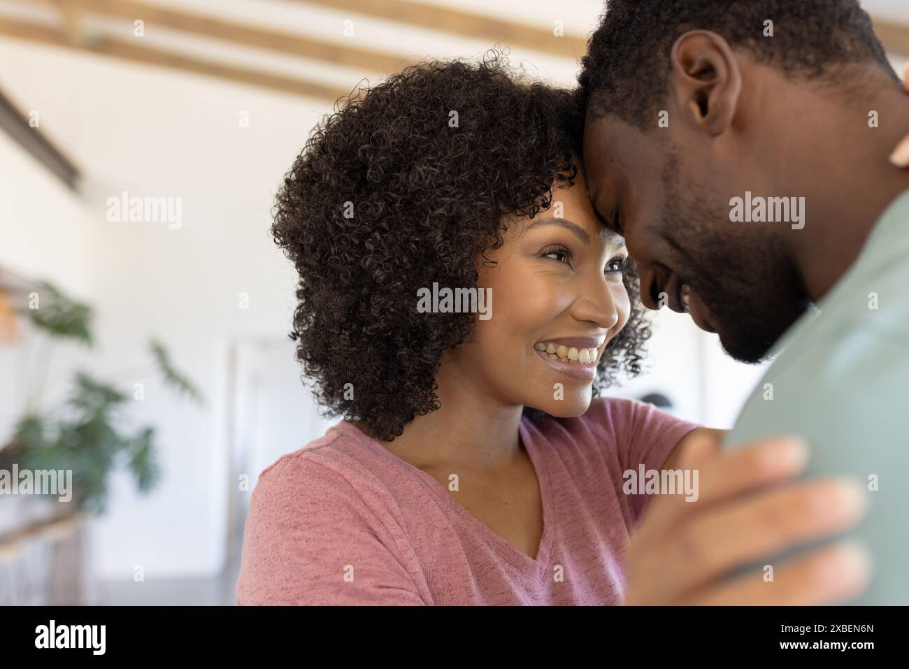 Una giovane donna birazziale sorride, abbracciando il suo partner in un salotto accogliente e ben illuminato Foto Stock