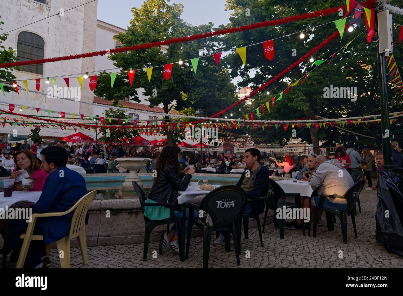 Le persone si godono pasti e bevande al jardim da grazia durante le popolari festività dei santi, seduti sotto gli ombrelloni colorati e sagres Foto Stock