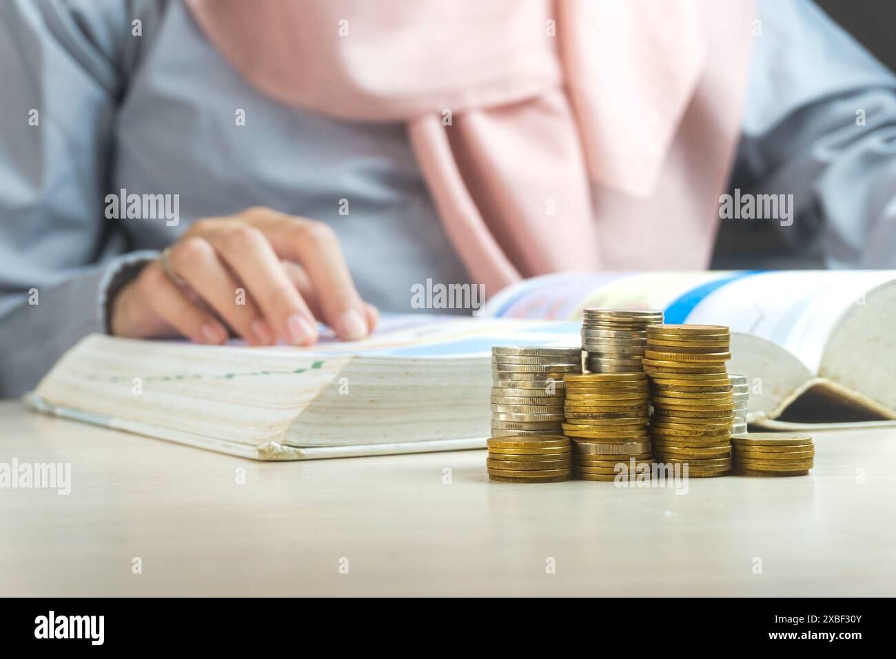 donna d'affari musulmana che legge un libro con un mucchio di monete moneta sul fronte simbolo per imparare la sharia il dividendo degli investimenti bancari finanziari da busine Foto Stock