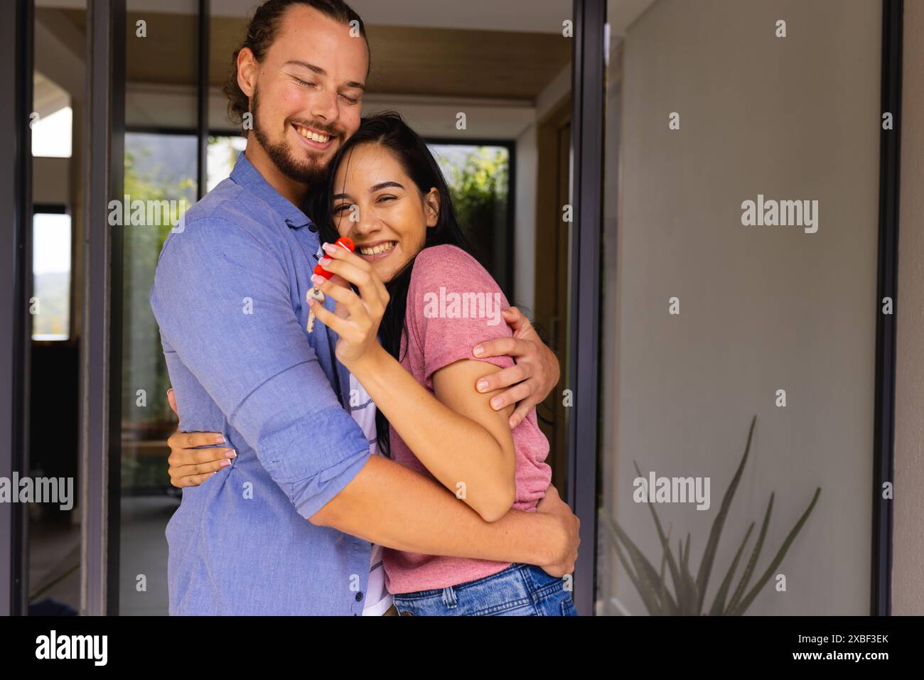 Diverse giovani coppie si abbracciano e sorridono tenendo in mano una chiave, acquistando prima casa Foto Stock