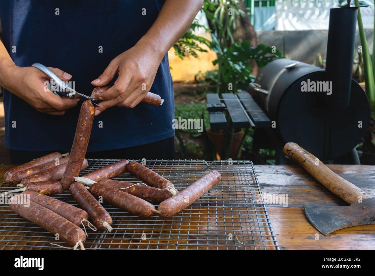 Un uomo sta tagliando una salsiccia che utilizza involucro di collagene, sarà cucinato utilizzando la tecnica di affumicatura Foto Stock