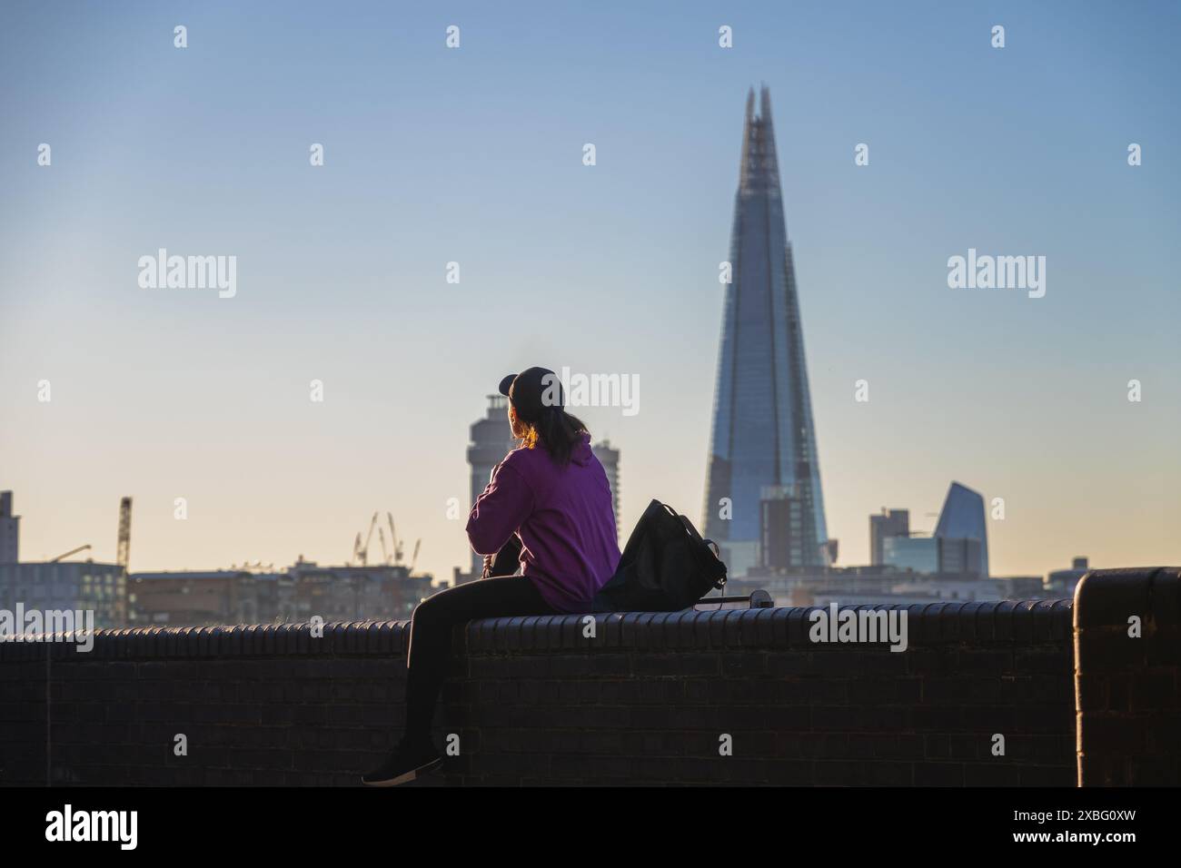 Vista posteriore di una donna seduta sul terrapieno del Tamigi con lo Shard sullo sfondo Foto Stock