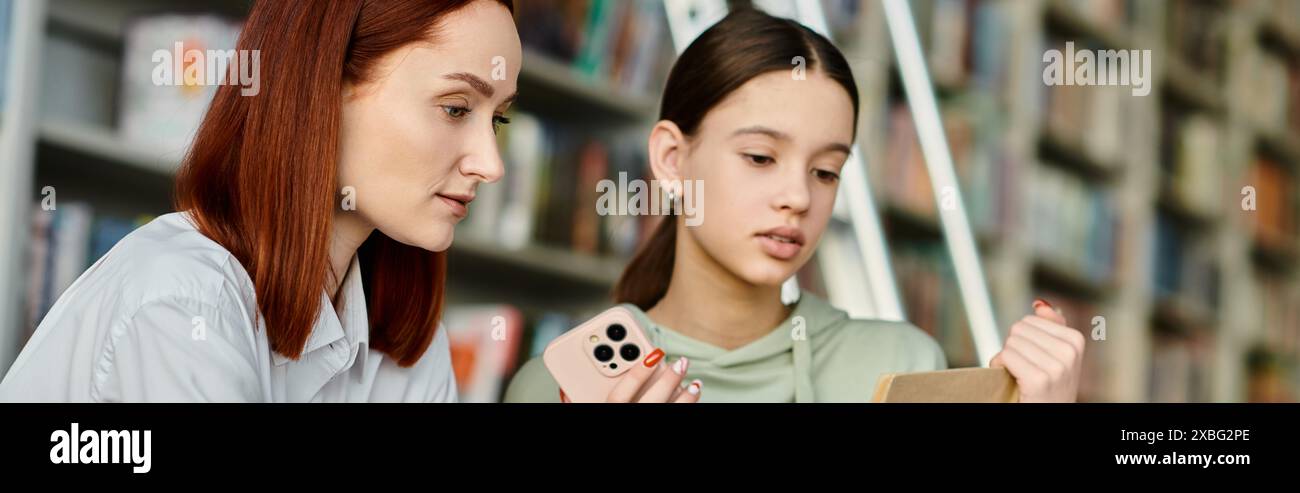 un tutor rosso e una ragazza adolescente, invischiati nei loro telefoni in una biblioteca. Foto Stock