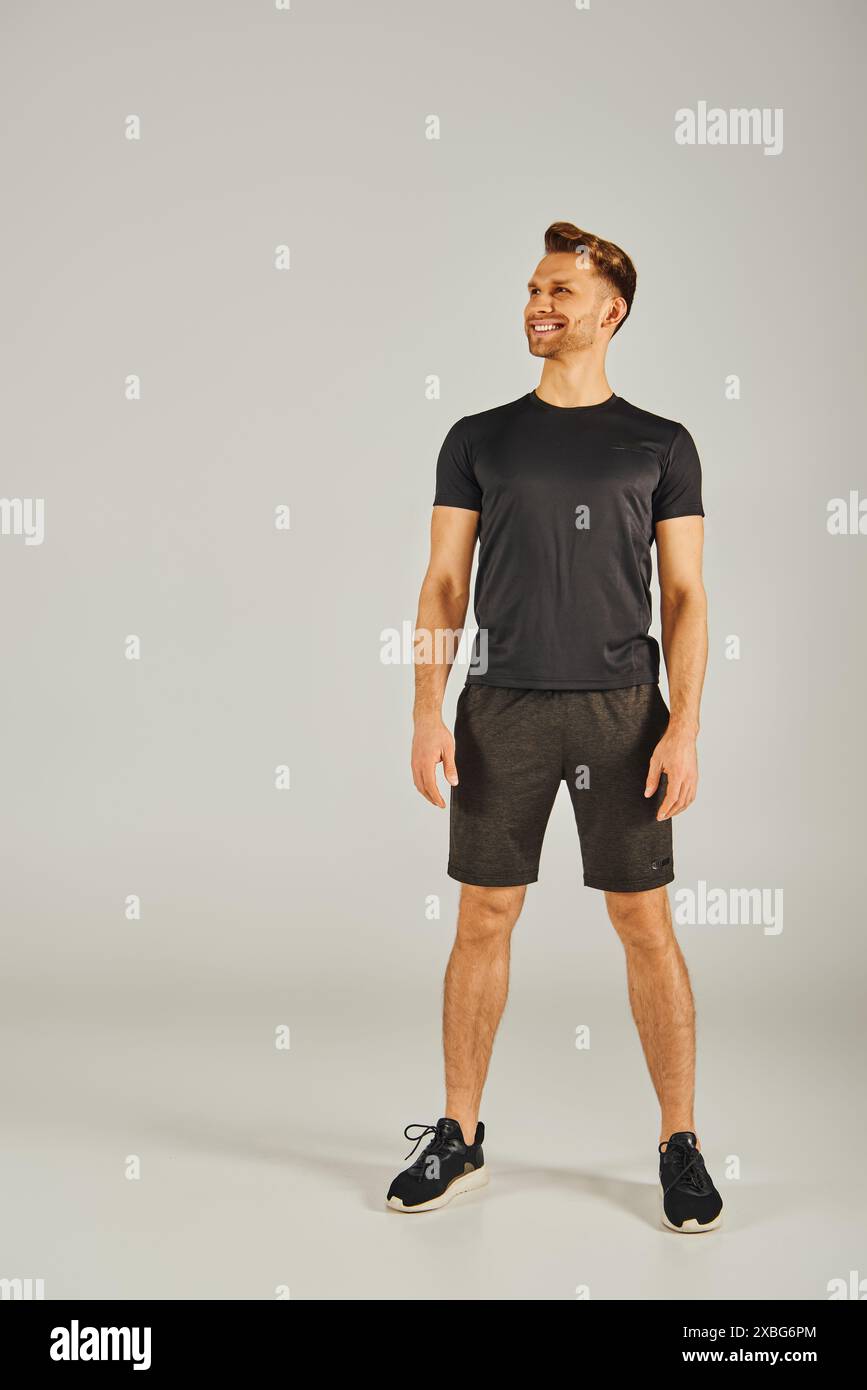 Un giovane atletico che indossa una t-shirt nera e pantaloncini corti e si allena in uno studio su uno sfondo grigio. Foto Stock