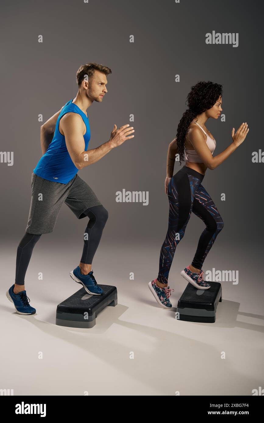 Una giovane coppia multiculturale con abbigliamento attivo che corre energicamente sugli stepper in un ambiente da studio. Foto Stock