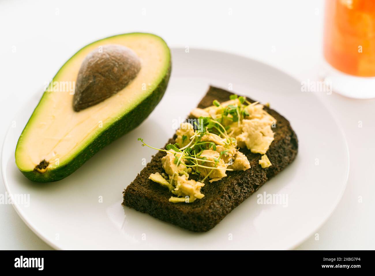 Fetta o tosta il pane di segale su un piatto con guacomole con microverdure, mezzo avocado su un piatto bianco e succo d'arancia su uno sfondo chiaro. Healt Foto Stock