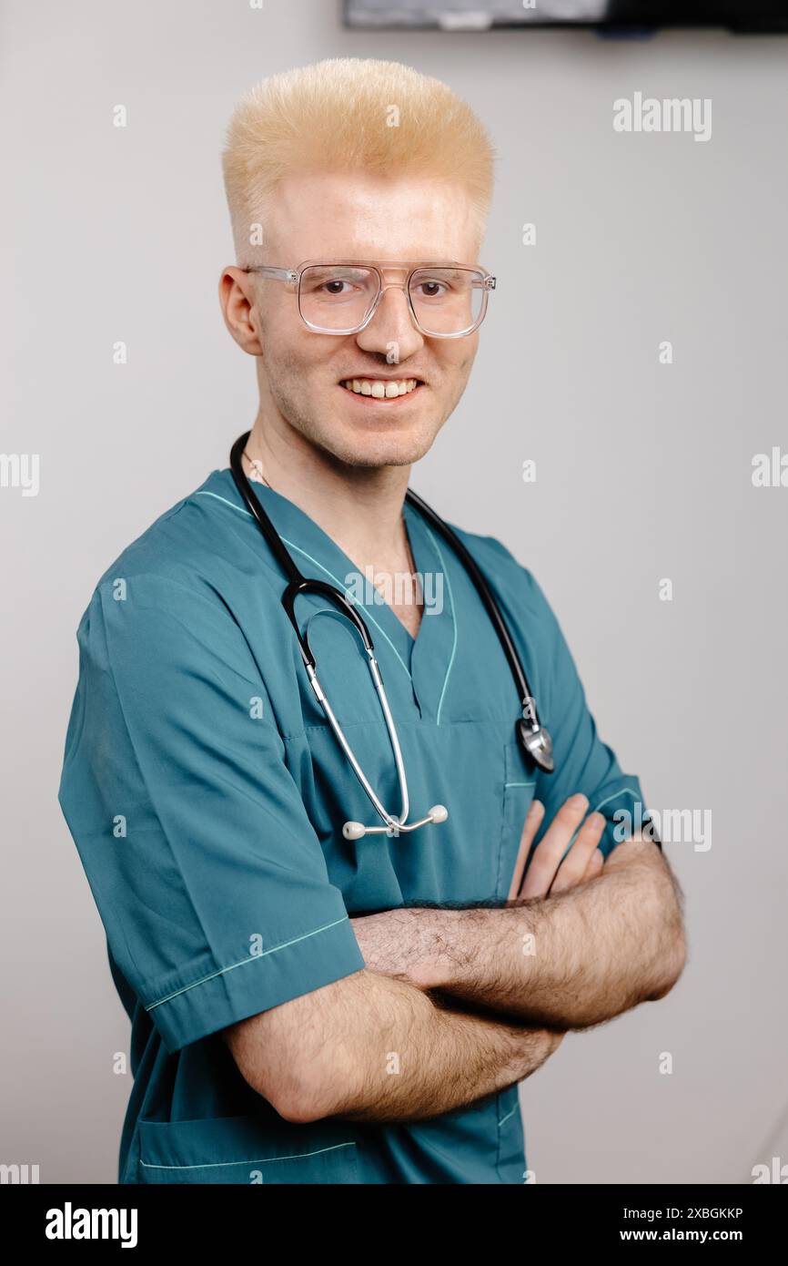 Un medico maschile in un telo scrub e uno stetoscopio sorride per la fotocamera. Foto Stock