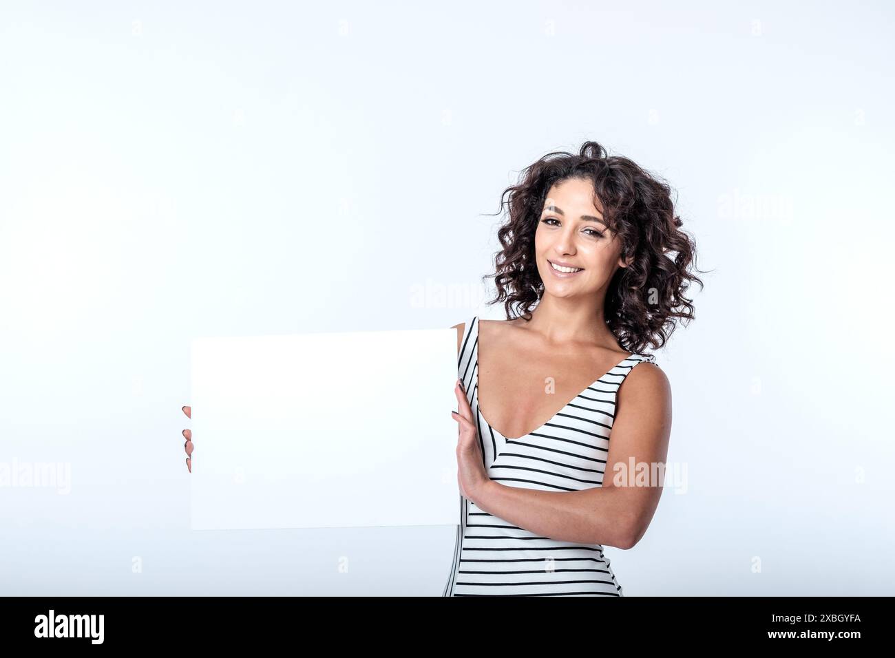 Bella donna mediterranea sorridente sui suoi 20 anni con un cartello con spazio per una copia dell'annuncio su sfondo bianco. L'immagine ha molto spazio di copia Foto Stock