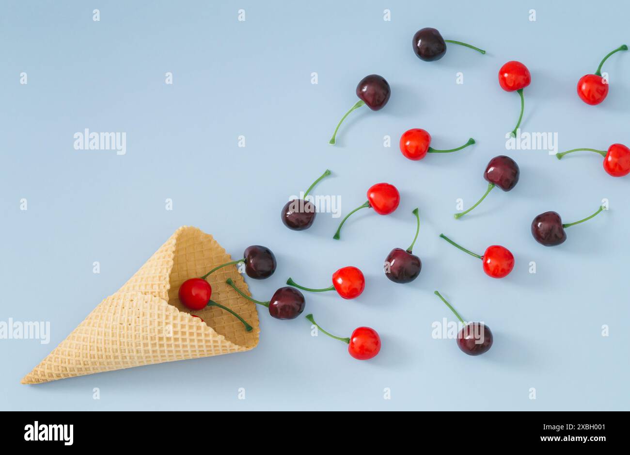 Ciliegie rosse che escono dal cono gelato waffle su sfondo azzurro. Concept creativo estivo minimalista. Gelato alla moda e ciliegia. Foto Stock