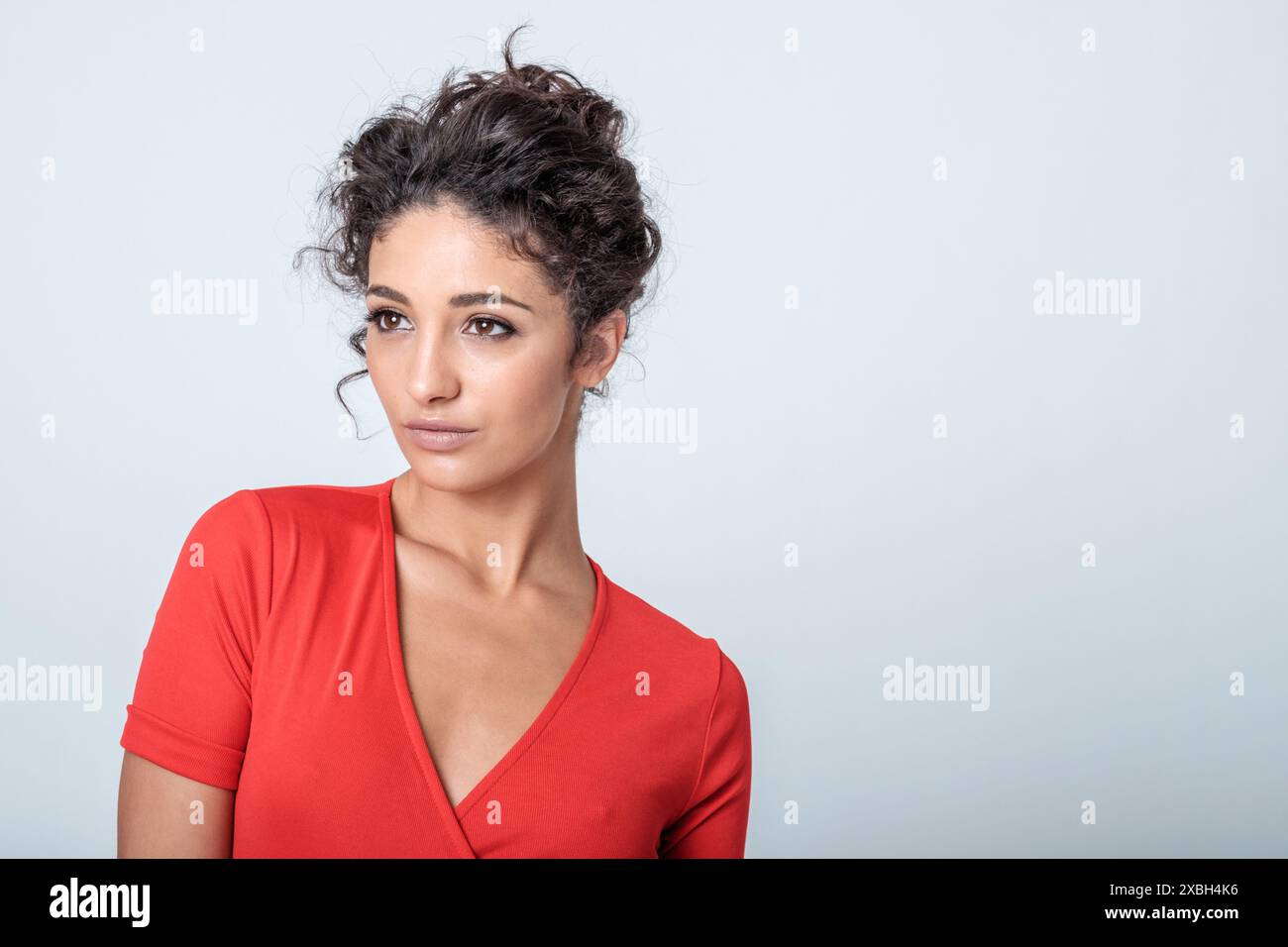 Una donna straordinariamente bella a metà degli anni '20 indossa un semplice abito rosso per un look elegante e disinvolto in questo scatto alla moda da studio contro una bg bianca Foto Stock