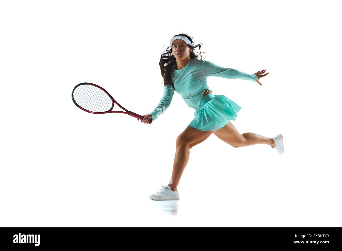 Tennista donna in costume verde menta si prepara a tornare al tiro, la sua espressione è focalizzata sullo sfondo bianco dello studio. Foto Stock