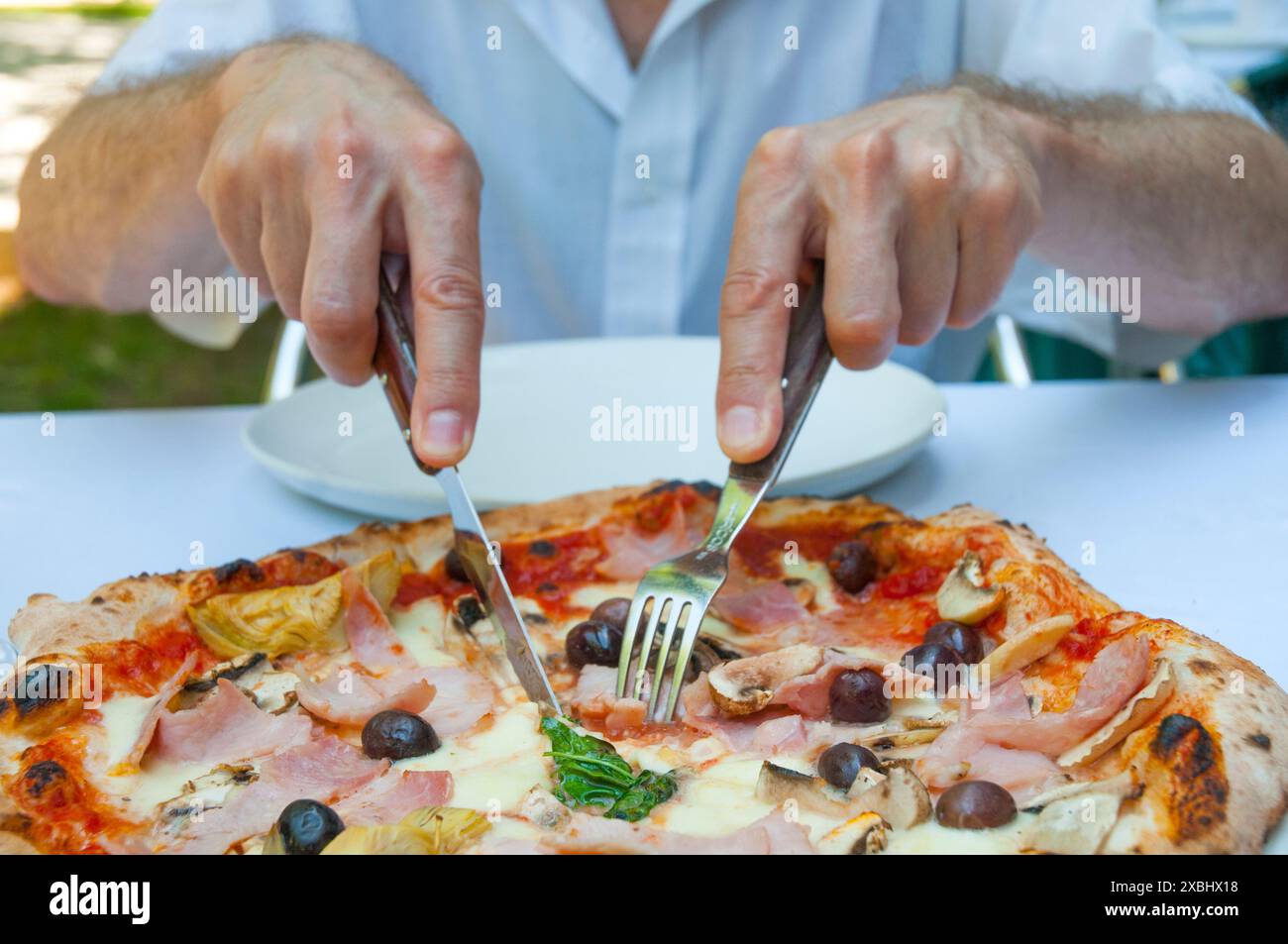 Le mani di un uomo tagliano un pezzo di pizza Capricciosa. Vista ravvicinata. Foto Stock