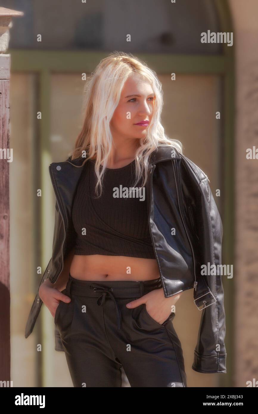La giovane donna indossa un modello 3/4 e indossa un outfit di tendenza in pelle con una camicia di pancia che sottolinea la sua affinità alla moda e la sua fiducia in se stessa. Foto Stock