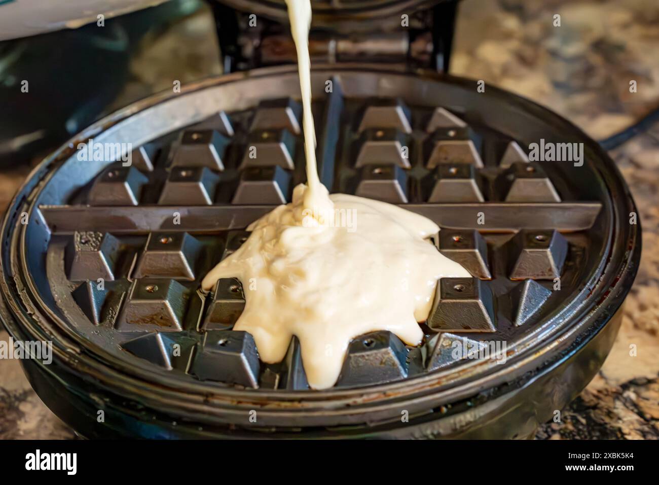 Aggiunta dell'impasto per waffle a una macchina elettrica calda per waffle. Foto Stock