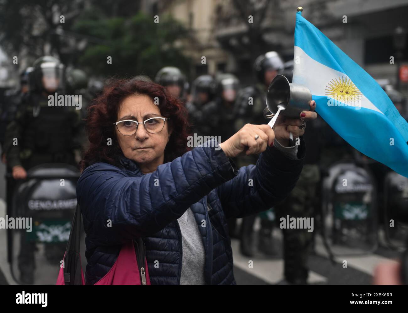 Buenos Aires, Argentina. 12 giugno 2024. Una donna con una bandiera argentina sbatte su una pentola di fronte a una fila di poliziotti durante una dimostrazione contro un progetto di riforma del governo ultraliberale. Credito: Fernando Gens/dpa/Alamy Live News Foto Stock