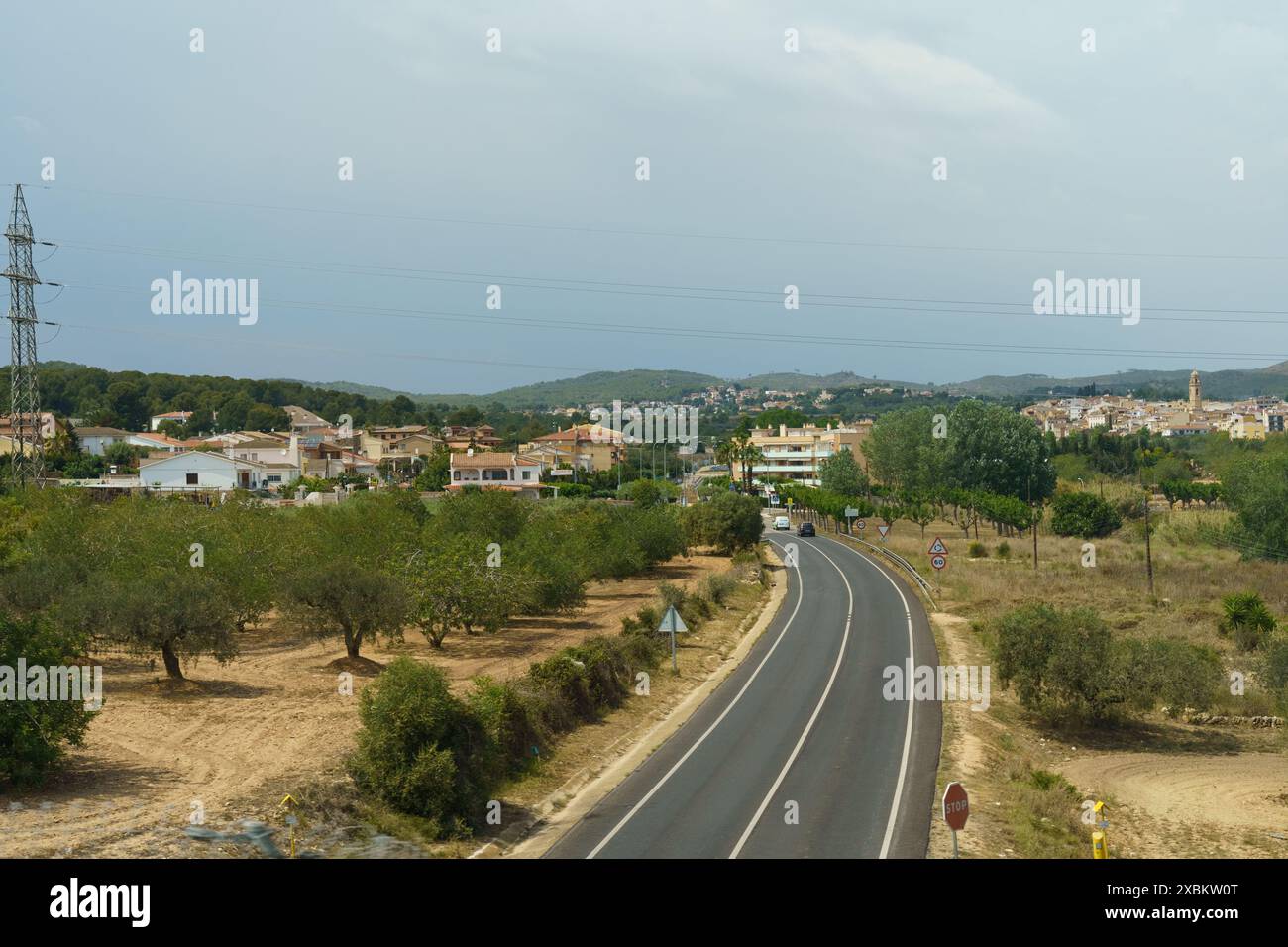 Una foto che mostra una strada asfaltata che serpeggia attraverso la campagna spagnola, con un lontano villaggio annidato tra le colline. Foto Stock