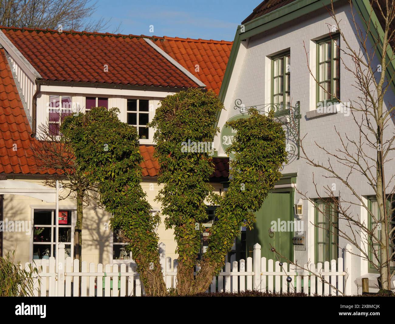 Case con giardini ben curati e una recinzione bianca davanti a loro in condizioni di sole, greetsiel, frisia orientale, germania Foto Stock