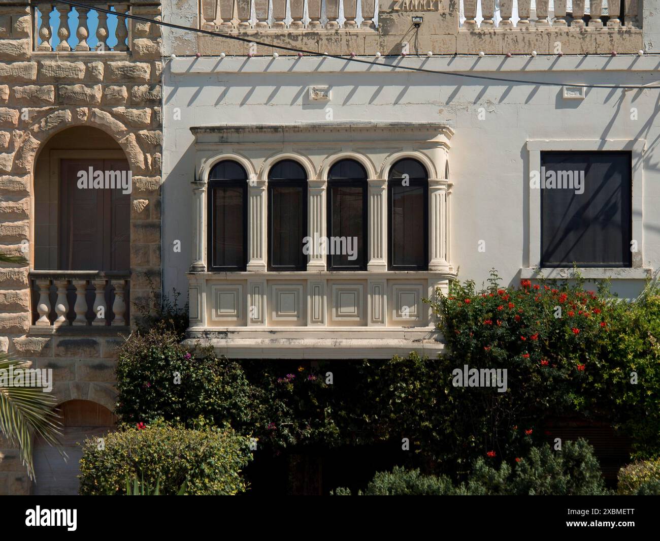 Casa tradizionale con balcone ornato e piante fiorite nel giardino, accanto a un muro di ciottoli, gozo, Mar mediterraneo, malta Foto Stock