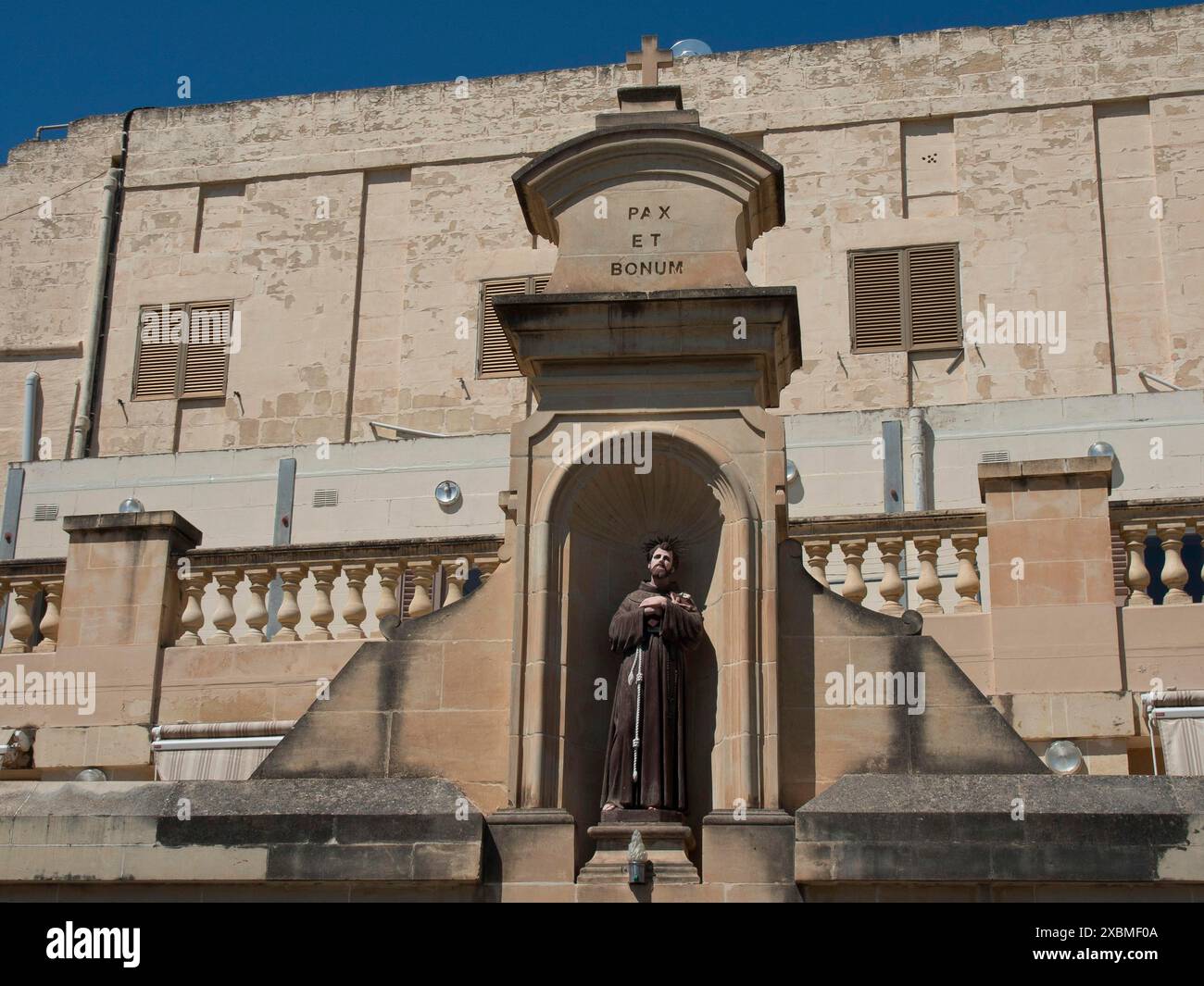 Statua di un monaco in una nicchia di pietra di fronte a un edificio storico, muro di pietra con iscrizione Pax et Bonum, gozo, Mar mediterraneo, malta Foto Stock
