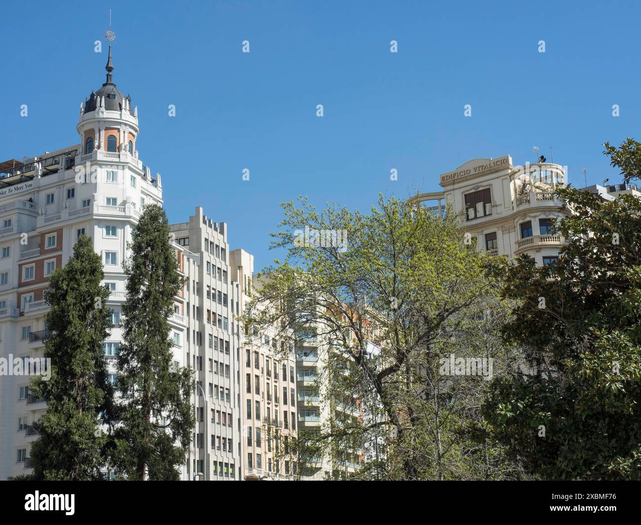 Diversi edifici dall'architettura diversa nell'area urbana, circondati da alberi verdi sotto un cielo azzurro, Madrid, Spagna Foto Stock