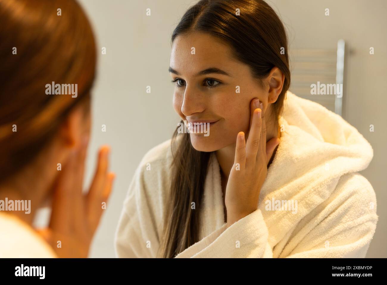 Donna caucasica sorridente in abito bianco che tocca il suo volto, guardando allo specchio Foto Stock