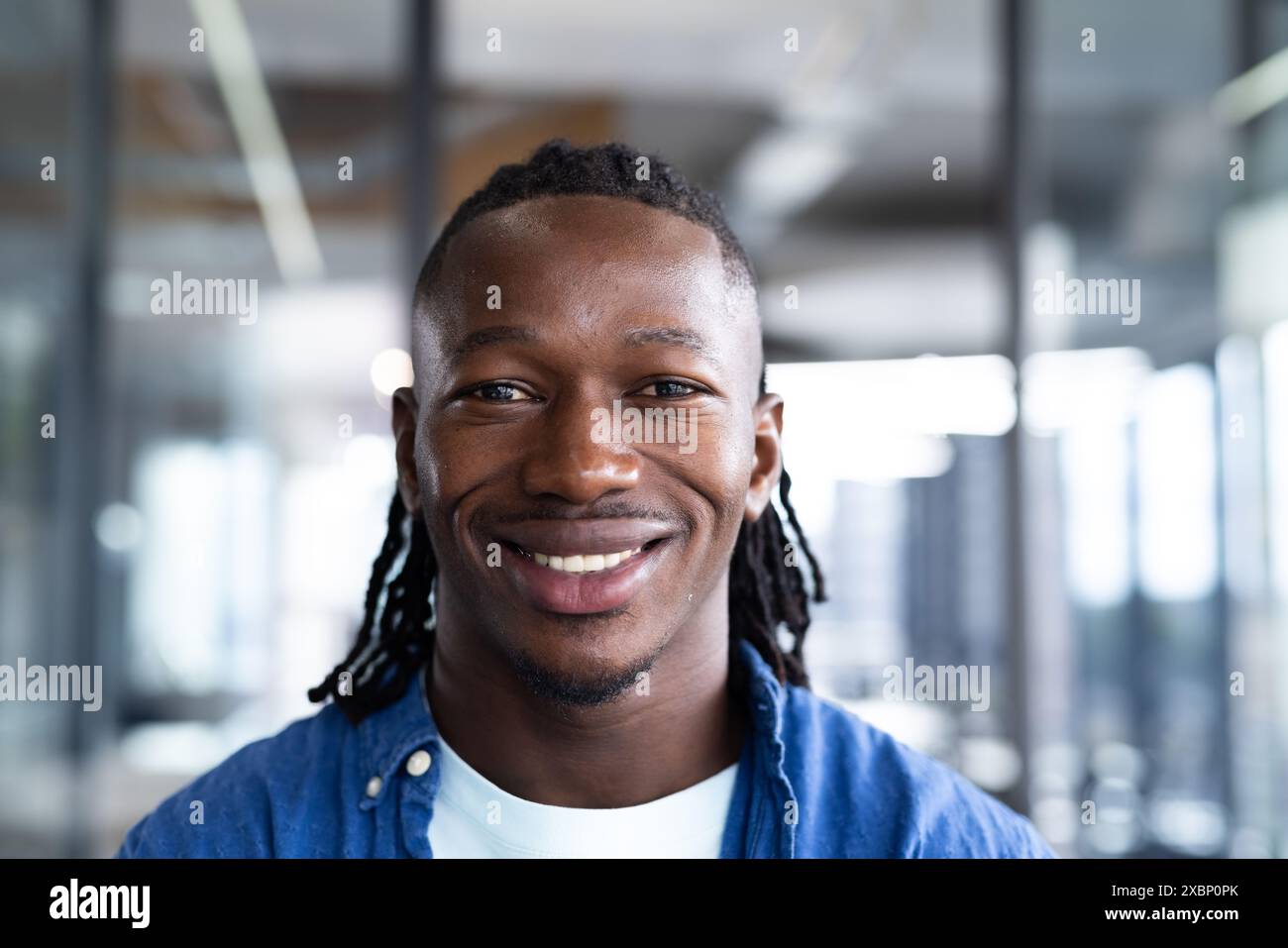 Giovane afroamericano sorridente in un ambiente d'ufficio con pareti di vetro, affari Foto Stock